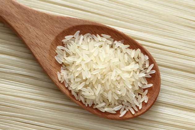 Rice in a wooden spoon on rice noodles background. Close-up.